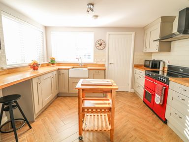 A kitchen with wooden countertops a red oven a movable wooden island and a wall clock at Cranny Corner in Carnlough