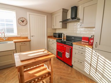 A kitchen with wooden countertops a red stove a wooden island and a clock on the wall at Cranny Corner in Carnlough