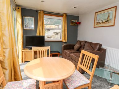 A dining area with round wooden table and chairs a brown sofa a TV on a wooden stand and paintings on walls at The Hen Pen in Star near Cenarth