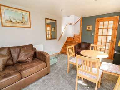 A living room with a brown sofa a round wooden dining table with four chairs a staircase a framed picture and a mirror on the wall at The Hen Pen in Star near Cenarth