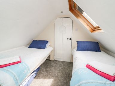A bedroom with two single beds under sloped ceilings and a small door at the end at The Hen Pen in Star near Cenarth