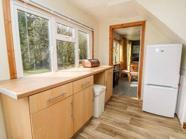 A kitchen with wooden cabinets a bread box a white refrigerator and a view into a dining area at The Hen Pen in Star near Cenarth