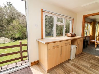 A kitchen area with wooden cabinets and a bread box near a window and a door opening to a garden at The Hen Pen in Star near Cenarth
