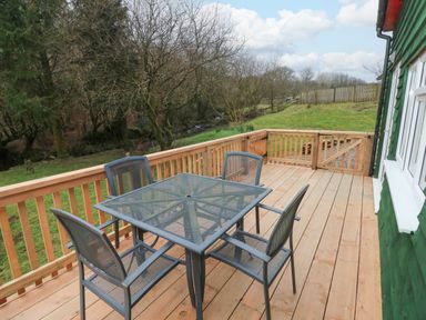 An outdoor wooden deck with a metal table and four chairs overlooking trees and grass at The Hen Pen in Star near Cenarth