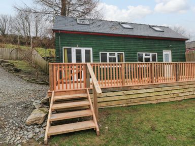 A green wooden house with a slate roof and wooden deck with stairs in front at The Hen Pen in Star near Cenarth