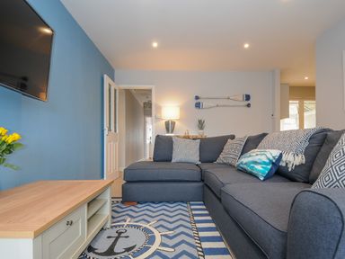 A living room with a blue sofa patterned cushions a rug with an anchor a wooden coffee table and oars on the wall at Coastal Haven Crackington near Crackington Haven