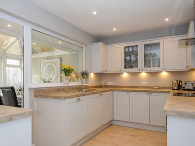 A kitchen with white cabinets wooden countertops under cabinet lights and flowers on the windowsill at Coastal Haven in Crackington near Crackington Haven