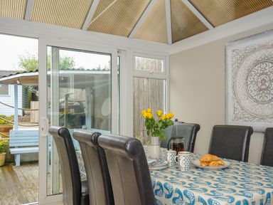 A dining area with a table covered with a blue and white patterned cloth and chairs around it at Coastal Haven in Crackington near Crackington Haven