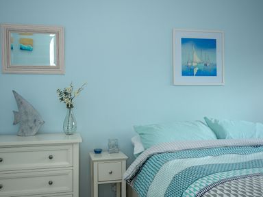 A bedroom with a bed, pillows and blankets next to a dresser and nightstand with decorations at Coastal Haven in Crackington near Crackington Haven