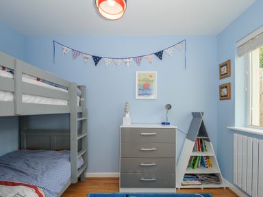 A children's bedroom with bunk beds a chest of drawers and a triangular bookshelf at Coastal Haven in Crackington near Crackington Haven