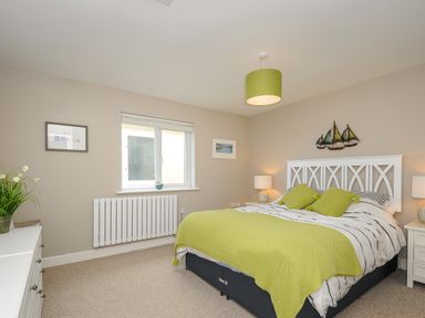 A bedroom with a double bed with green cushions and blanket and a white dresser with a plant at Coastal Haven in Crackington near Crackington Haven