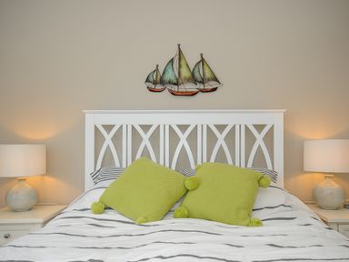 A bed with green cushions and striped bedding with lamps on bedside tables and a sailboat decoration on the wall at Coastal Haven in Crackington near Crackington Haven