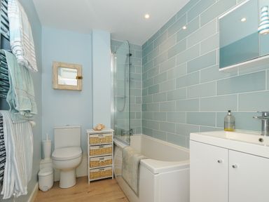 A bathroom with a toilet, a bathtub with shower, a small drawer unit, a sink with cabinet, and towels hanging at Coastal Haven in Crackington near Crackington Haven