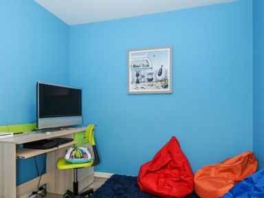 A room with a television on a desk a green chair with a cushion and three bean bags on a blue rug at Coastal Haven in Crackington near Crackington Haven