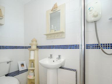 A bathroom with a toilet sink mirror wooden lighthouse shelf and shower at Coastal Haven in Crackington near Crackington Haven