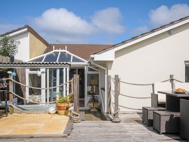 An outdoor deck area with wooden flooring and patio furniture in front of a conservatory at Coastal Haven in Crackington near Crackington Haven