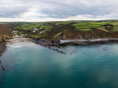 A coastal landscape with rocky shoreline green fields and scattered houses at Coastal Haven in Crackington near Crackington Haven