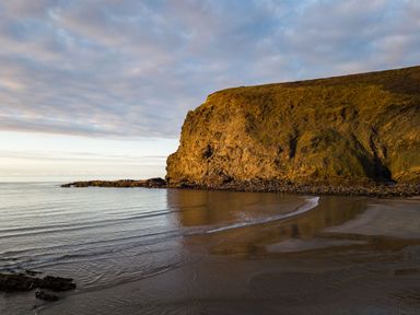 A rocky cliff beside calm sea water and sandy shore at Coastal Haven in Crackington near Crackington Haven