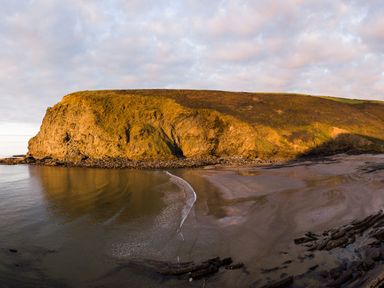 A coastal landscape with a cliff, rocky shore, and sandy beach at Coastal Haven in Crackington near Crackington Haven