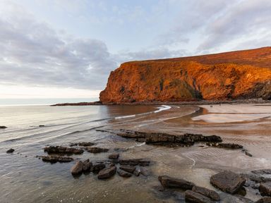 A beach with rocks in the water and a large cliff in the background at Coastal Haven in Crackington near Crackington Haven