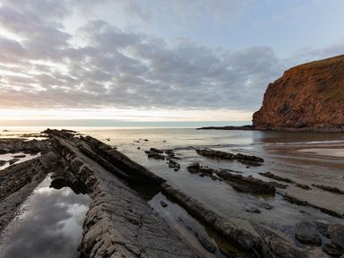 A rocky coastline with water and a cliff under a cloudy sky at Coastal Haven in Crackington near Crackington Haven
