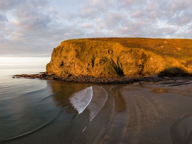A coastal scene with a large rocky cliff and a sandy beach at Coastal Haven in Crackington near Crackington Haven