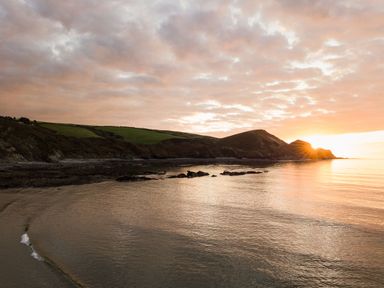 A coastal scene with hills and the sun setting over the water at Coastal Haven in Crackington near Crackington Haven