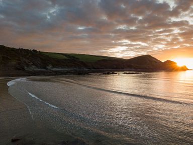A beach with gentle waves and hills at sunrise at Coastal Haven in Crackington near Crackington Haven