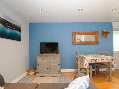 A living room with a television on a cabinet and a dining table with chairs at Coastal Haven in Crackington near Crackington Haven