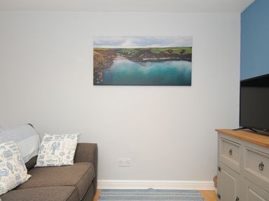 A living room with a gray sofa with printed cushions a TV on a cabinet and a landscape photo on the wall at Coastal Haven in Crackington near Crackington Haven