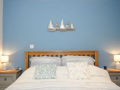 A bedroom with a wooden bed frame blue wall with sailing boat decoration bedside tables with lamps at Coastal Haven in Crackington near Crackington Haven