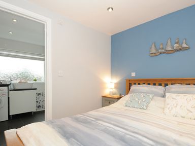 A bedroom with a wooden bed and bedside table with lamp next to an en suite bathroom at Coastal Haven in Crackington near Crackington Haven