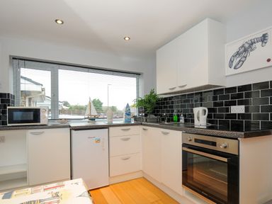 A kitchen with white cabinets black tile backsplash oven and a window with nautical decorations at Coastal Haven in Crackington near Crackington Haven