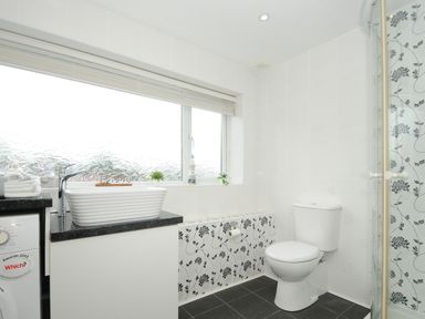 A bathroom with a toilet sink countertop washing machine and window with a blind at Coastal Haven in Crackington near Crackington Haven