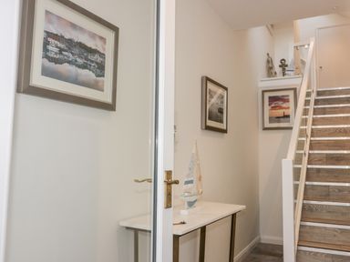 A hallway with a small table holding a decorative sailboat and framed pictures on the walls next to a staircase at Midships in Mevagissey