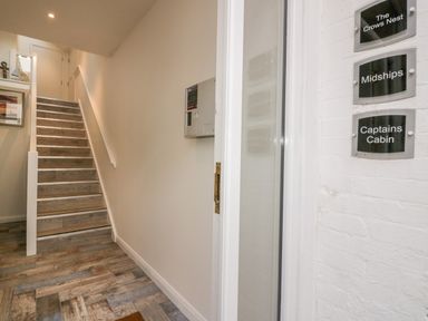 A hallway with wooden stairs leading up and name plaques on a white brick wall at Midships in Mevagissey