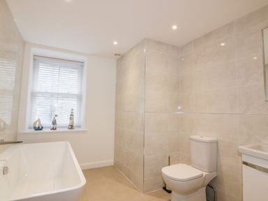 A bathroom with a bathtub toilet sink window and decorative items on the window ledge at Midships in Mevagissey