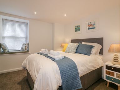 A bedroom with a double bed pillows and towels beside a window with cushions and a bedside table lamp at Midships in Mevagissey