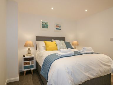A bedroom with a double bed blue and yellow cushions bedside tables with lamps and framed pictures on the wall at Midships in Mevagissey