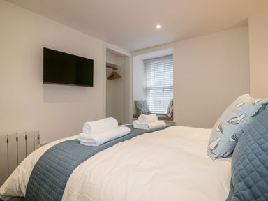 A bedroom with a bed a wall mounted TV and a window seat at Midships in Mevagissey