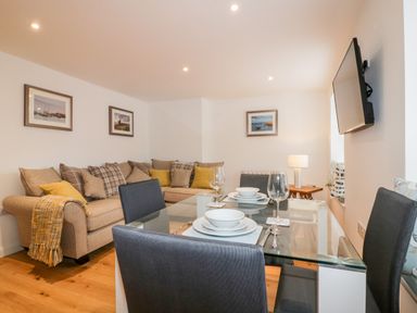 A dining area with a glass table set for four and a seating area with a sofa and cushions at Midships in Mevagissey