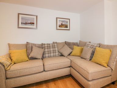 An L-shaped beige sofa with multiple cushions and two framed pictures on the wall at Midships in Mevagissey