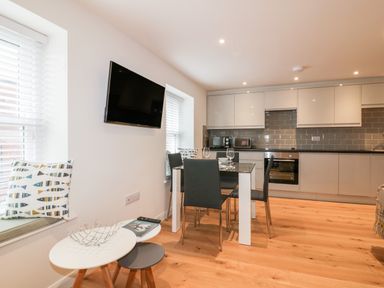 A kitchen with white cabinets a dining table with four chairs and a wall mounted TV at Midships in Mevagissey