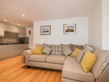 A beige sofa with yellow and plaid cushions in a living area next to a modern kitchen at Midships in Mevagissey