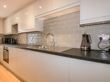 A kitchen with white cabinets a black countertop a stainless steel sink a kettle and a toaster at Midships in Mevagissey