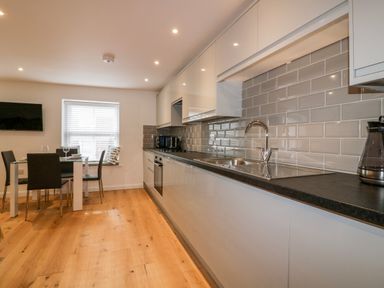 A kitchen with white cabinets black countertop dining table with chairs and a window at Midships in Mevagissey