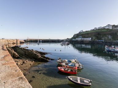 A harbor with several small boats tied near a stone pier and buildings on a hill at Midships in Mevagissey