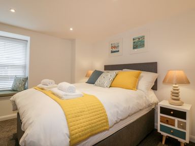 A bedroom with a bed with yellow and patterned pillows a bedside table with a lamp and a window seat with a cushion at The Crows Nest in Mevagissey
