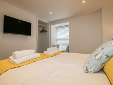 A bedroom with a mounted television towels on a bed and a window with blinds at The Crows Nest in Mevagissey