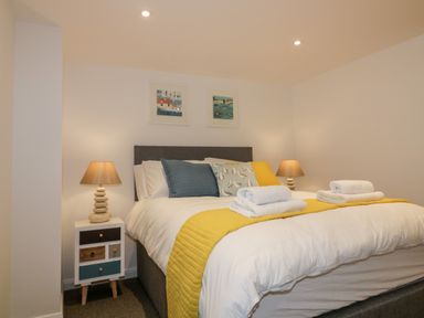 A bedroom with a double bed yellow bed runner and towels two bedside tables with lamps and artwork on the wall at The Crows Nest in Mevagissey